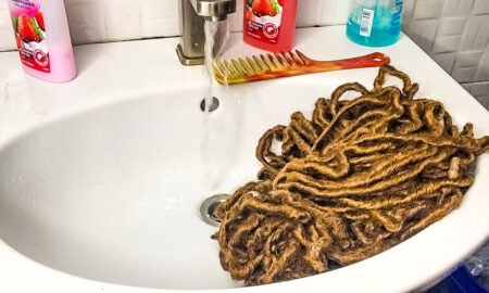 running water over crochet hair extesions surrounded by shampoo, conditioner and a comb on a water basin in a bathroom